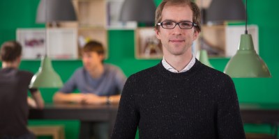 The CTO of a tech company in the foreground, with several lamps hanging behind him, in the background.