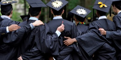 Students in graduation robes embracing with their backs to the camera.