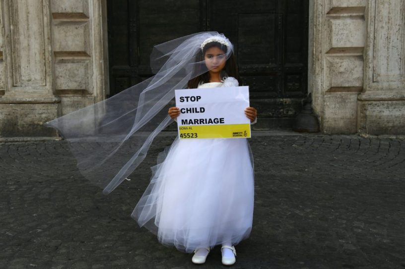 A child actress dressed as a child bride and holding a sign that says "Stop child marriage".
