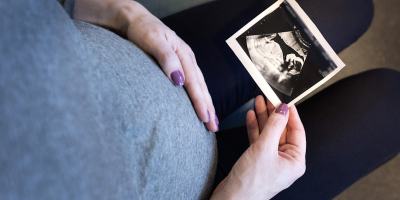 A pregnant woman touching her belly and looking at an image from a scan.
