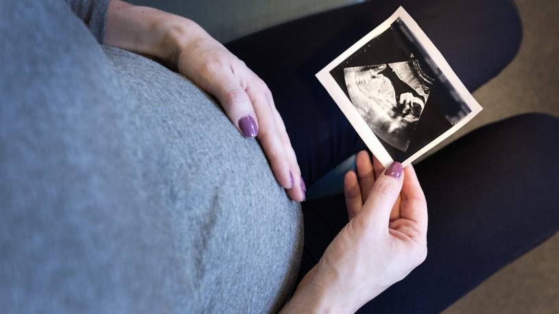 A pregnant woman touching her belly and looking at an image from a scan.